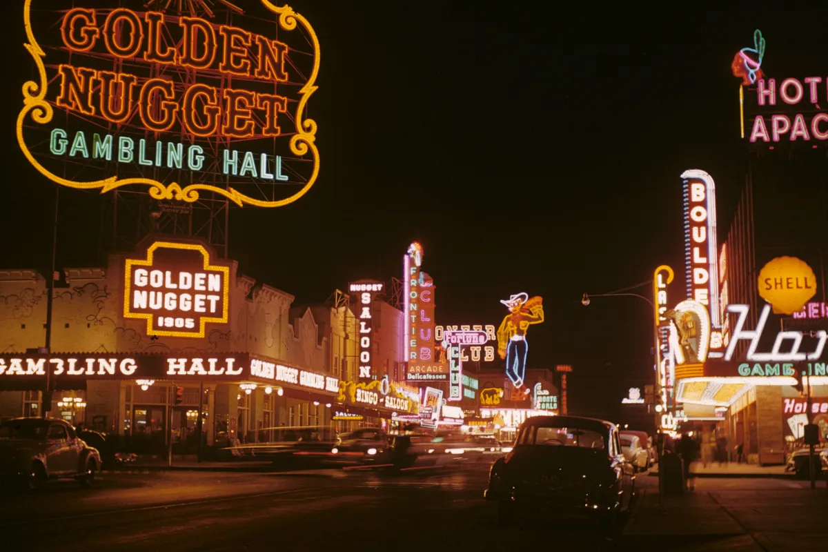 Color photograph of Fremont Street at night, glowing neon casino signs above old cars