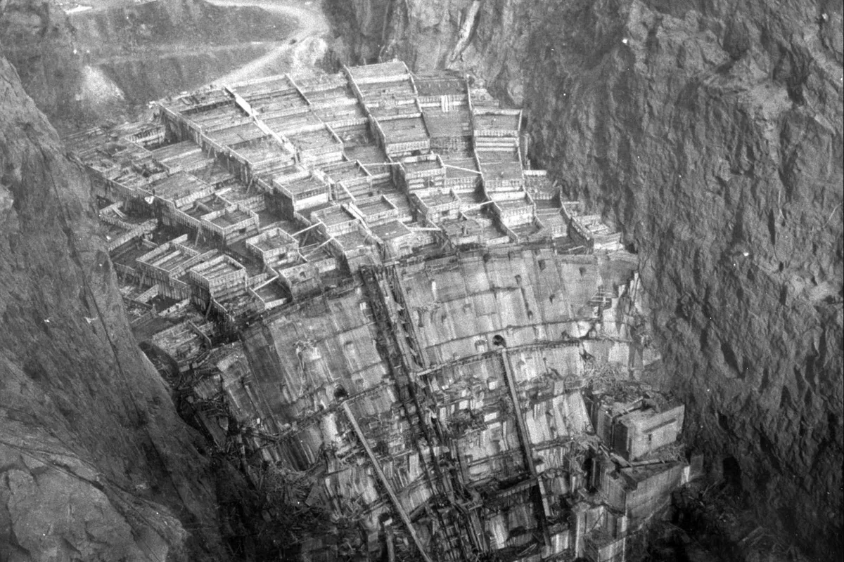 Black and white photograph of Hoover Dam rising in blocks of concrete between steep canyon walls