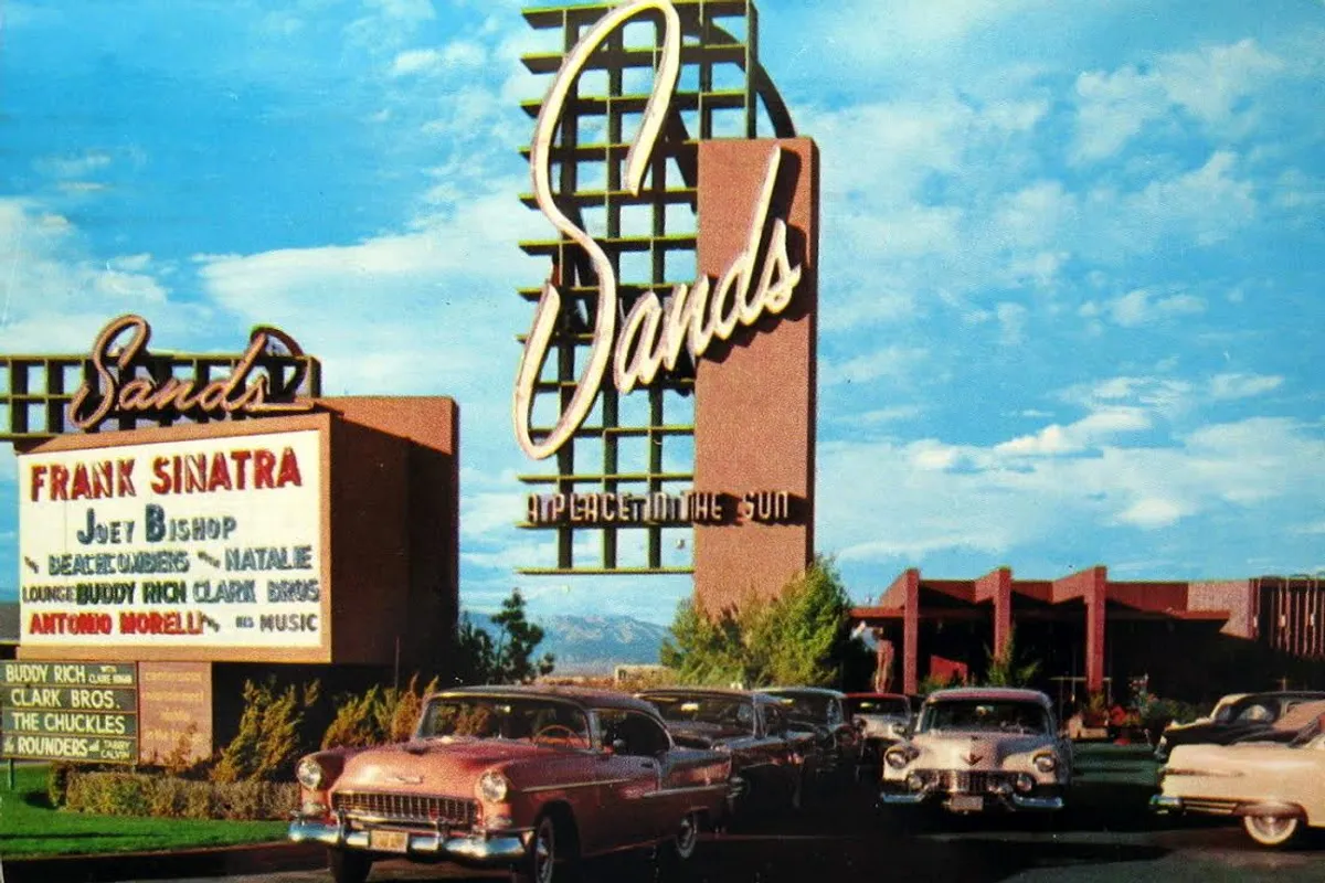 The tall Sands sign beside a marquee billing Frank Sinatra and Joey Bishop, finned cars parked in front