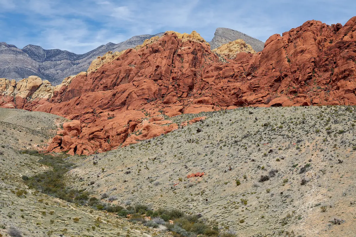 Red and cream sandstone hills rising above a dry desert slope under a blue sky