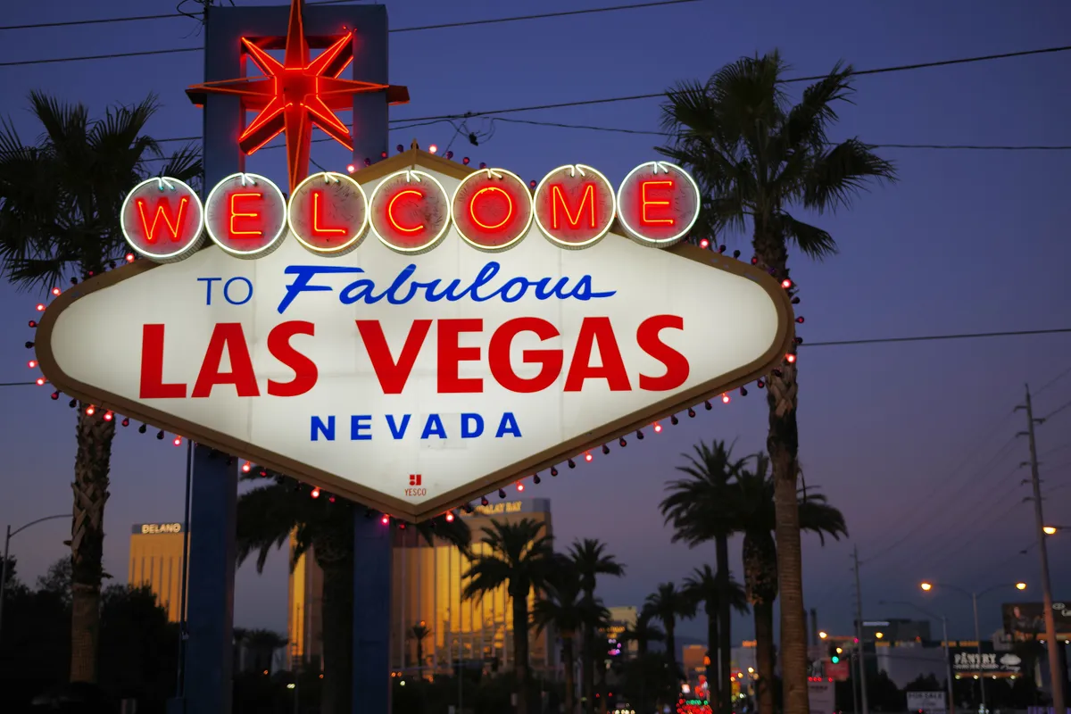 The Welcome to Fabulous Las Vegas sign lit at dusk, palm trees and hotel towers behind