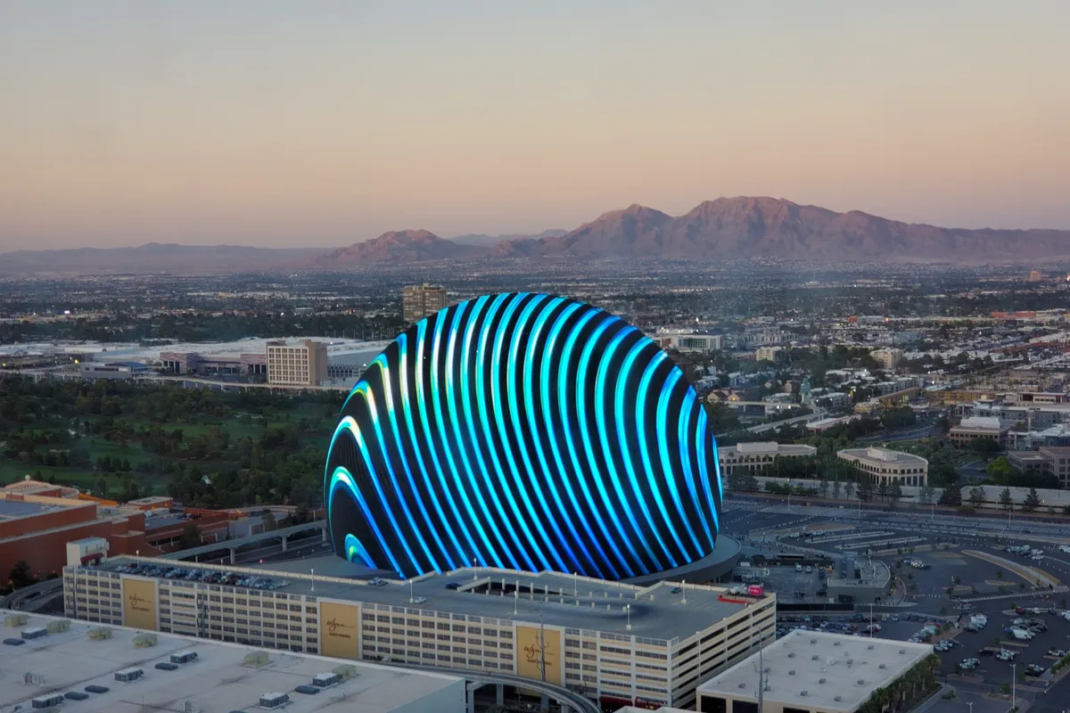 The Sphere glowing with curved blue stripes at dusk, seen from above, with desert mountains on the horizon