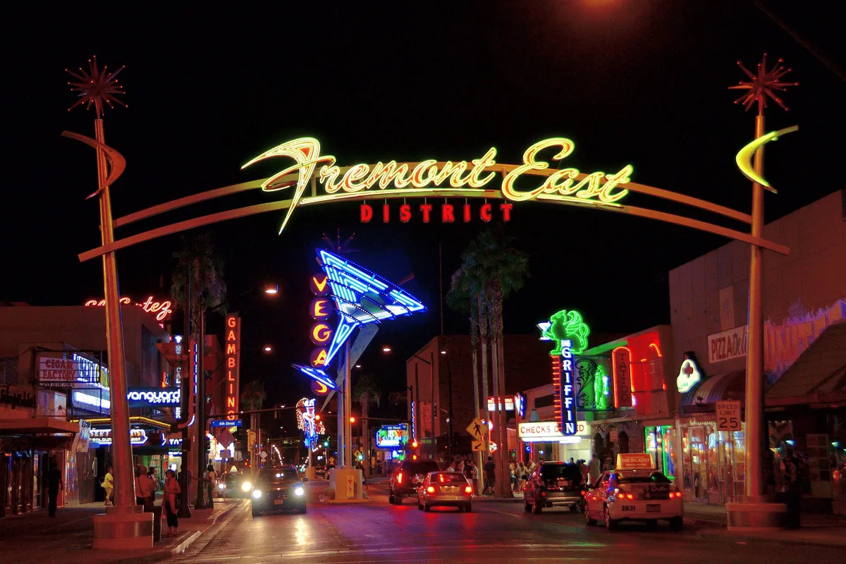 The neon arch of the Fremont East District over the street at night, a giant martini glass sign and glowing signs beyond