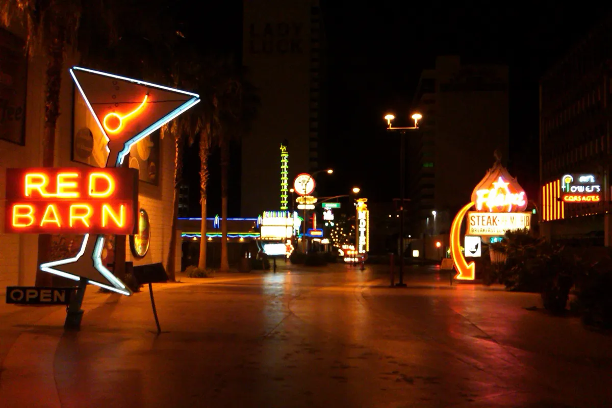 Restored vintage neon signs glowing along a dark pedestrian street, a Red Barn sign and a martini glass in front
