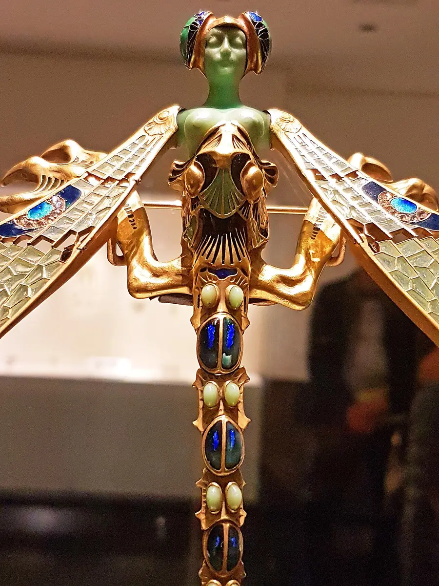 A gold and enamel corsage ornament of a woman with dragonfly wings