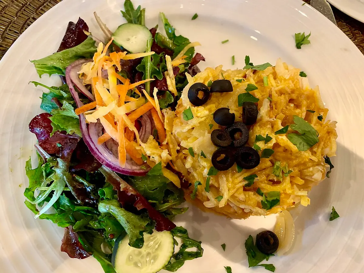 Bacalhau à Brás topped with black olives, next to a salad