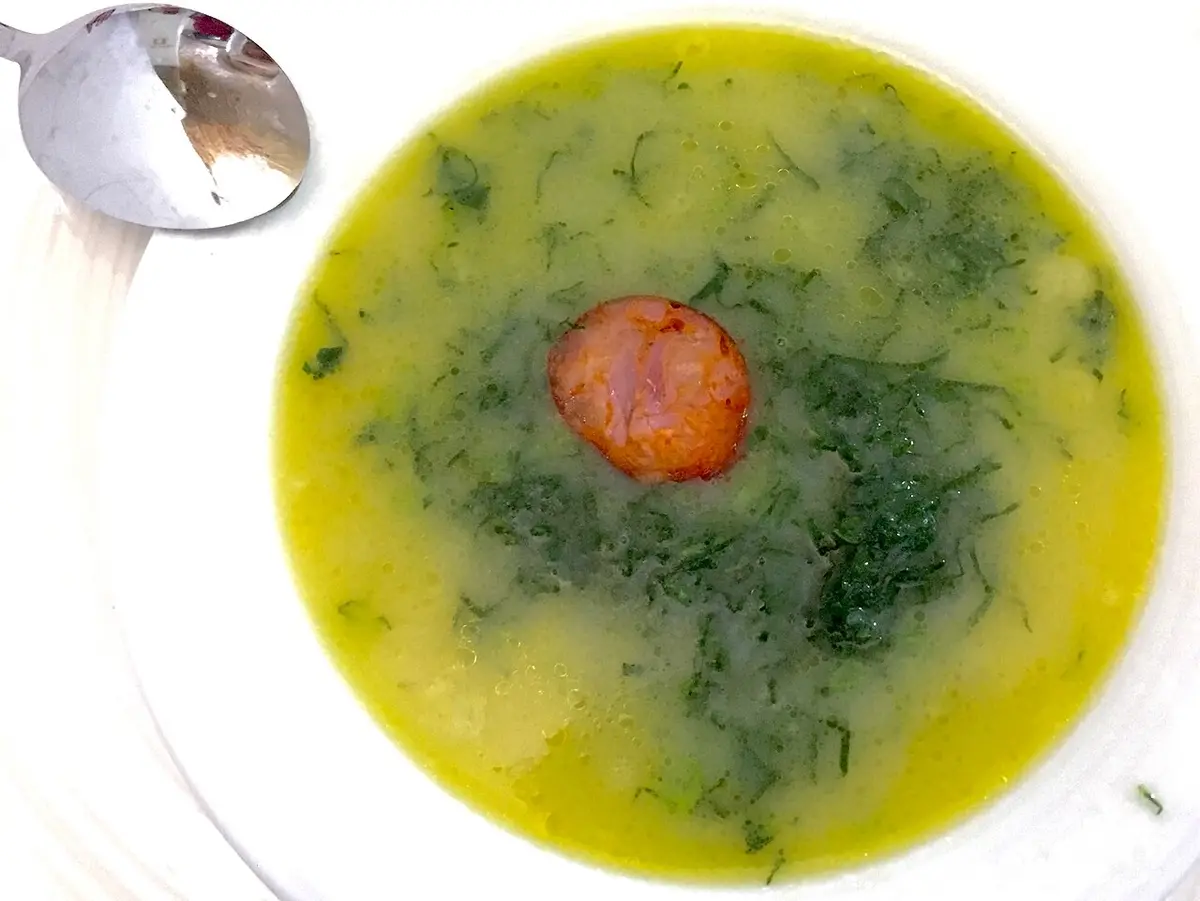 A bowl of caldo verde, green kale soup with a slice of chouriço