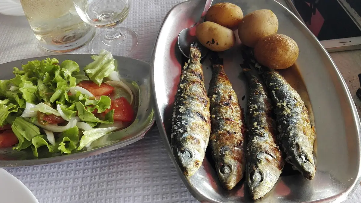 Grilled sardines on a metal platter with boiled potatoes, next to a salad