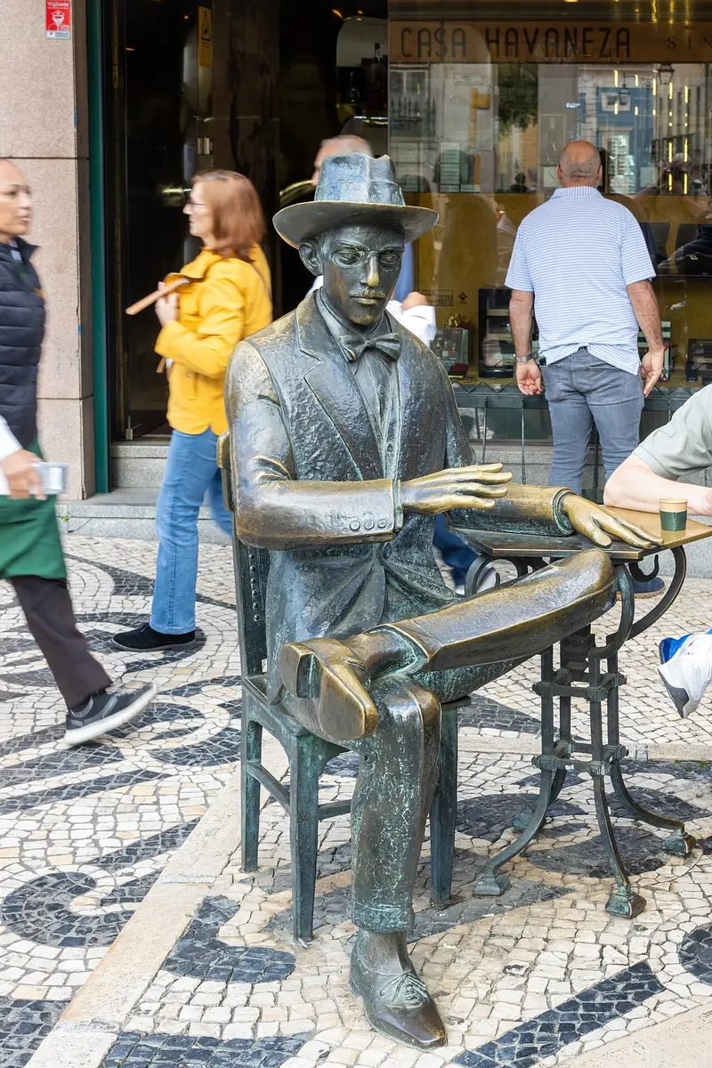 Bronze statue of Fernando Pessoa seated at a café table on a mosaic pavement