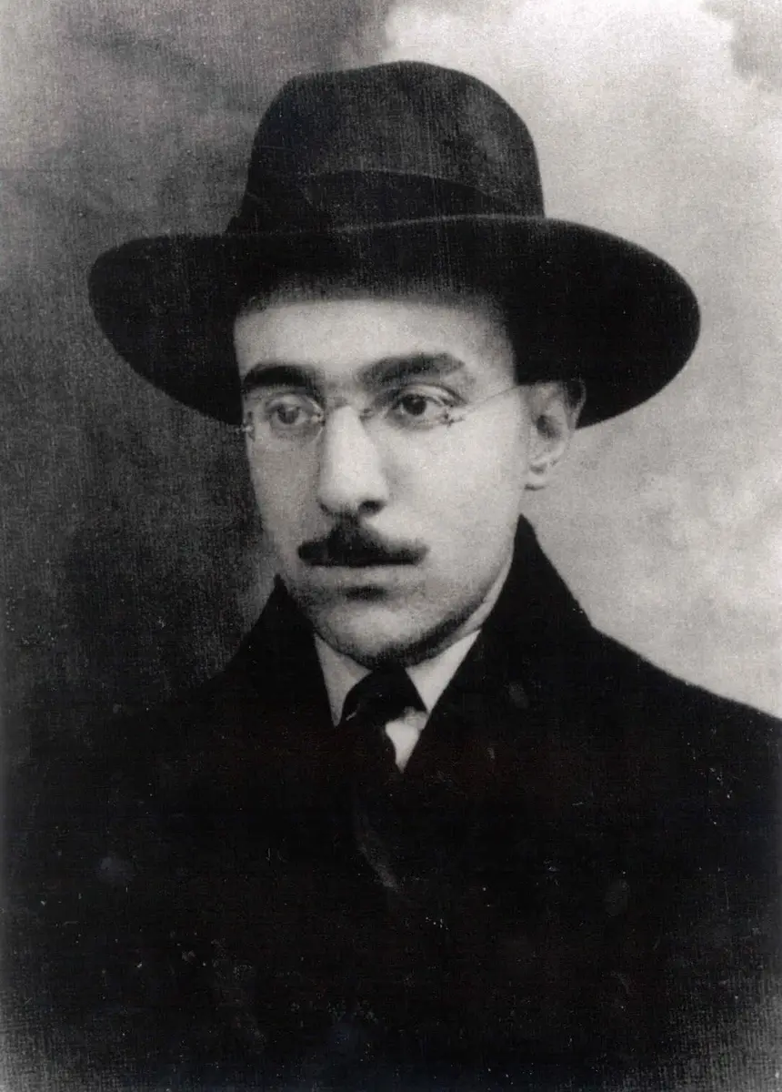 Black and white photograph of Fernando Pessoa in a hat and glasses