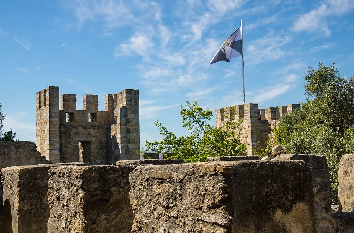 Crenellated towers of São Jorge Castle with a flag against a blue sky