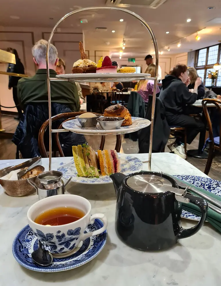 A tiered stand of sandwiches, scones and cakes beside a cup of tea and a teapot