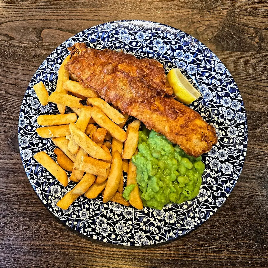 Battered fish with chips, mushy peas and a lemon wedge on a blue and white plate