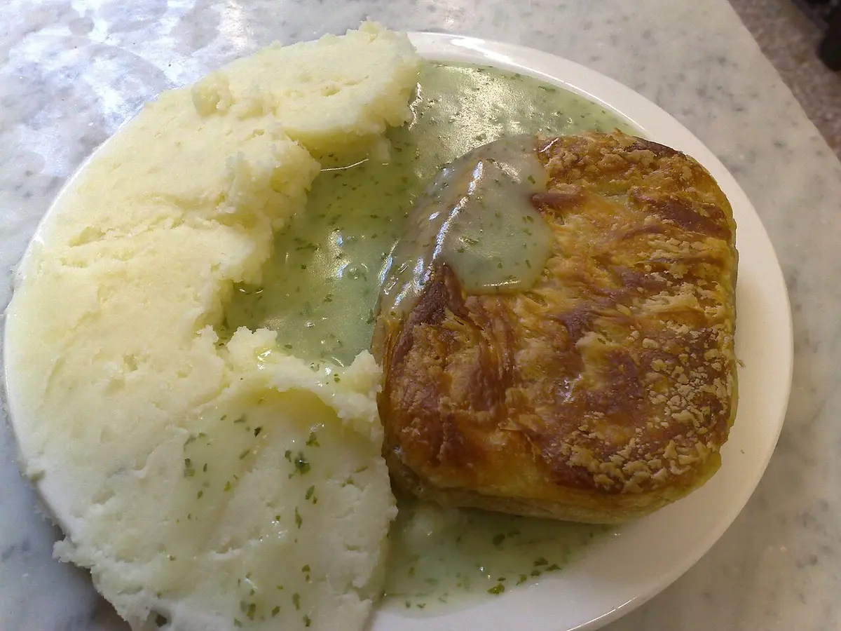 A pie with mashed potato and green parsley liquor on a white plate