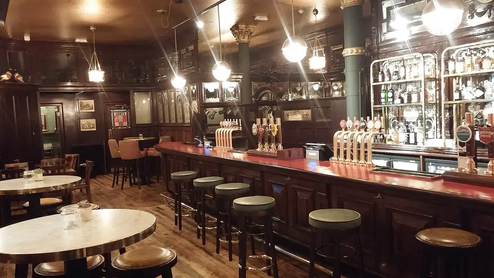 A Victorian pub interior with a long wooden bar, beer pumps and stools