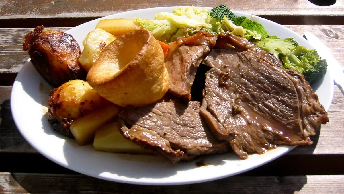 Slices of roast beef with a Yorkshire pudding, roast potatoes and greens