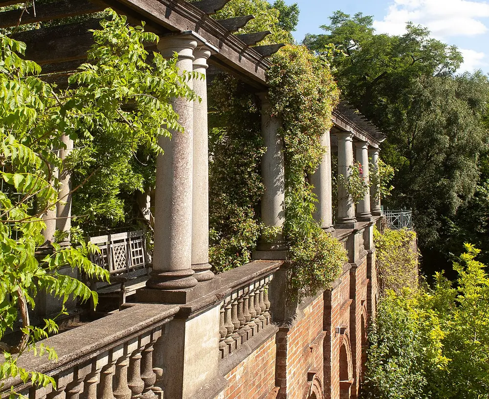 Stone columns of the Hampstead pergola hung with climbing plants above a brick terrace