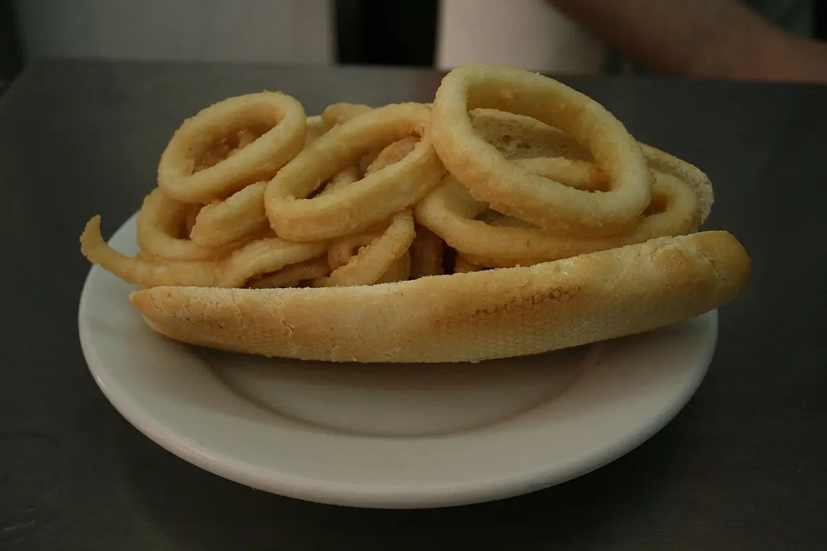 A bocadillo de calamares, fried squid rings in a bread roll, on a white plate