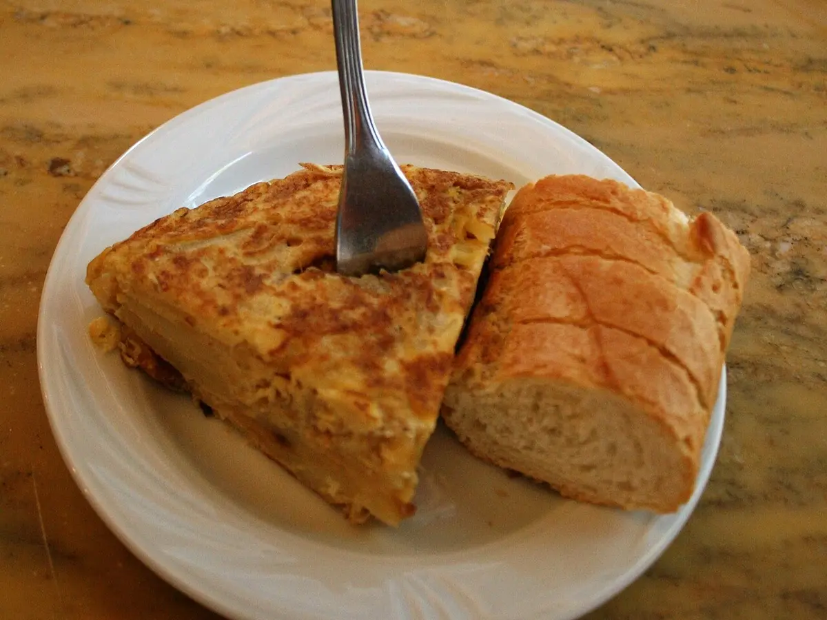 A wedge of Spanish potato omelet with a piece of bread on a bar counter