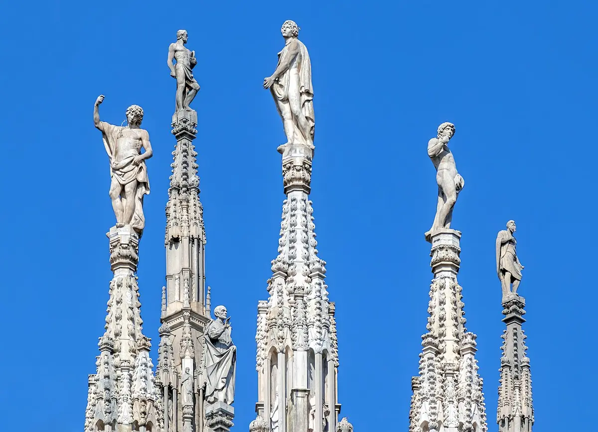 Marble statues standing on top of the Duomo’s spires against a blue sky