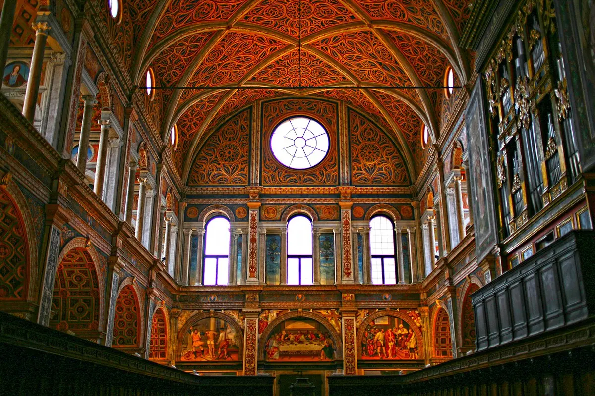 The frescoed hall of the nuns in San Maurizio, with a painted vault, a round window and an organ