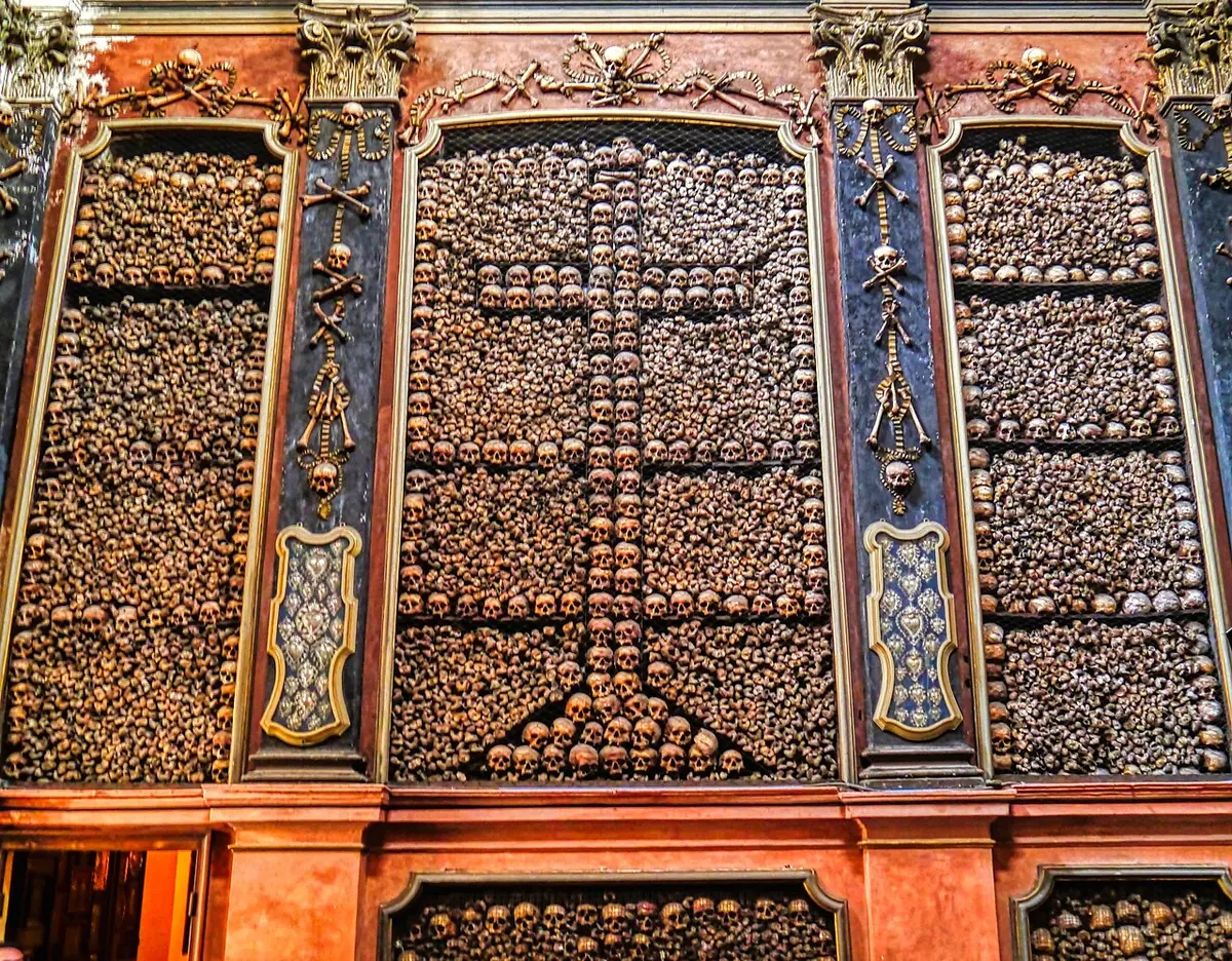 A wall of the ossuary of San Bernardino alle Ossa lined with skulls and bones, a cross of skulls in the center