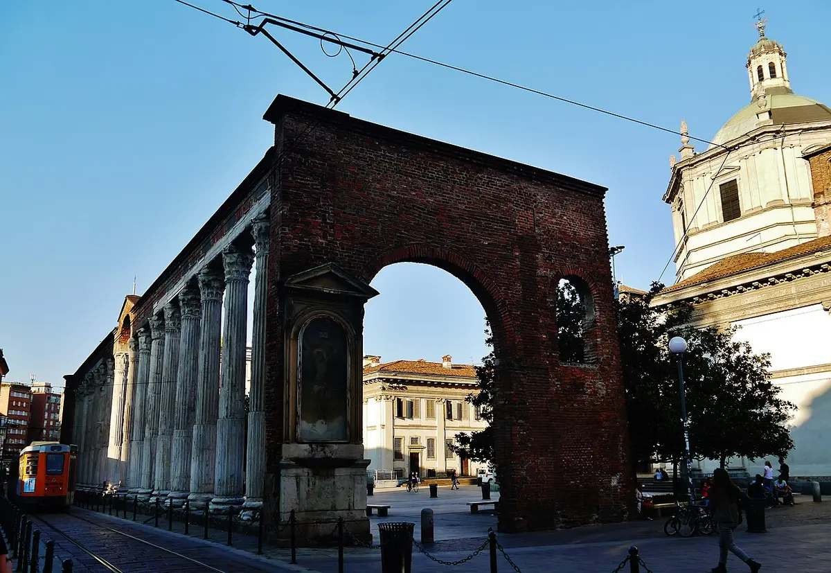 A row of Roman marble columns ending at a brick arch, with the dome of San Lorenzo behind