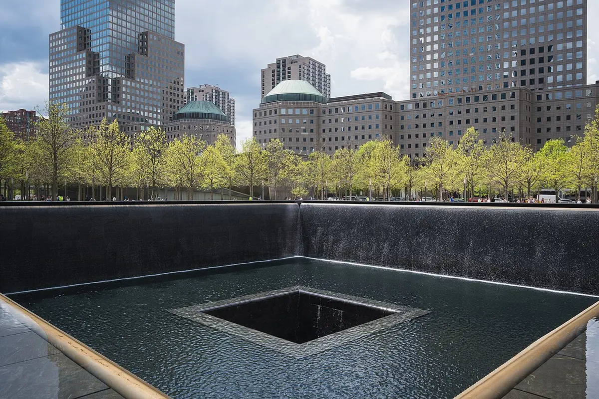 The north pool of the 9/11 Memorial, water falling into a square void, trees and towers behind