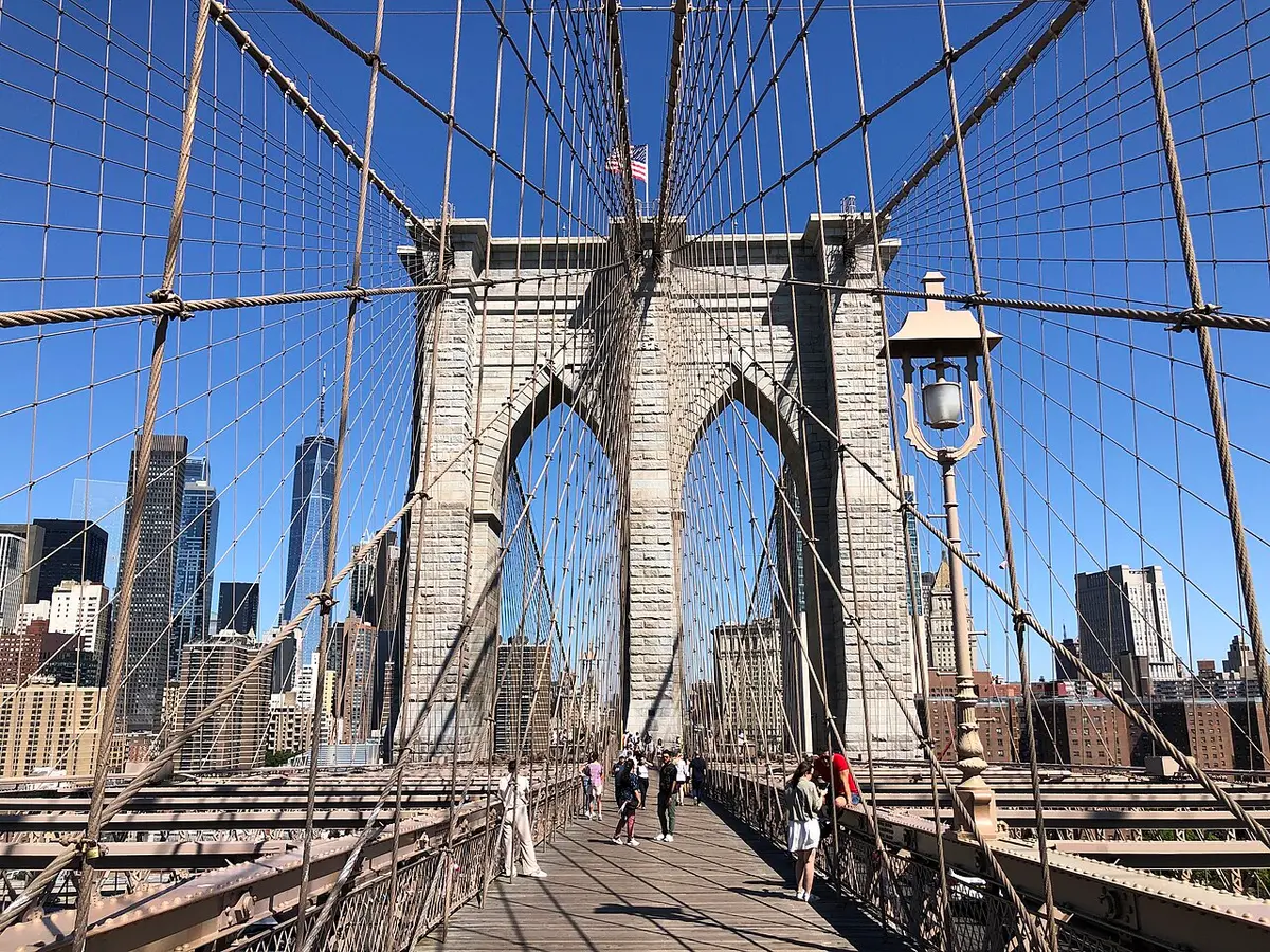 The wooden walkway of the Brooklyn Bridge running toward the stone Manhattan tower under a web of cables