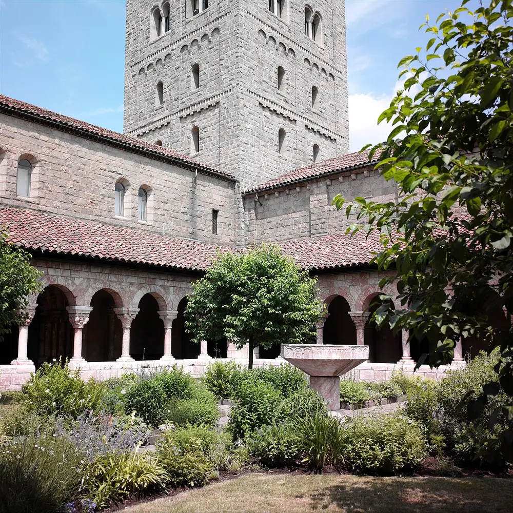 The garden of the Cuxa Cloister at the Met Cloisters, arcades of pink stone around it and a square tower above