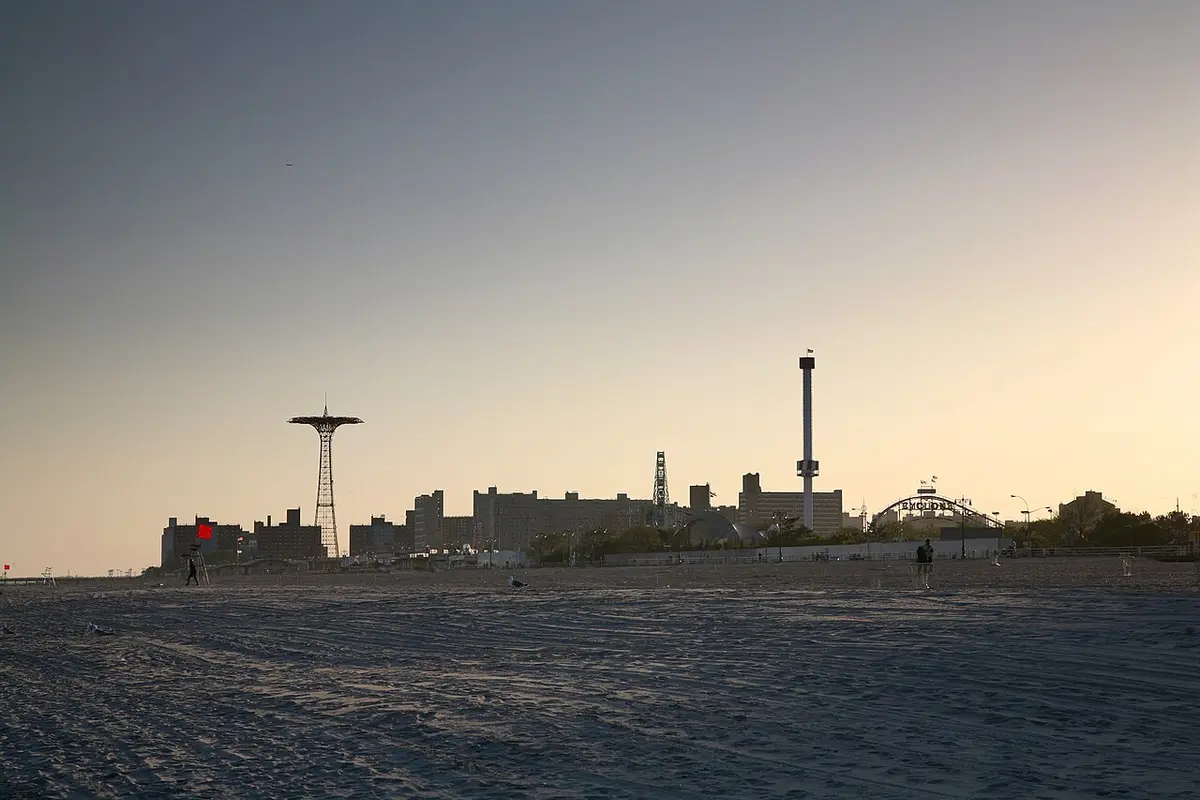 The wide sand beach at Coney Island before sunset, the Parachute Jump tower and rides on the skyline