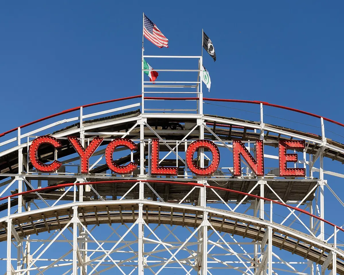 The red CYCLONE sign on top of the white wooden roller coaster, flags flying above it
