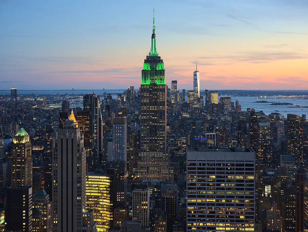 The Empire State Building lit green at dusk above the towers of Midtown, the harbor beyond