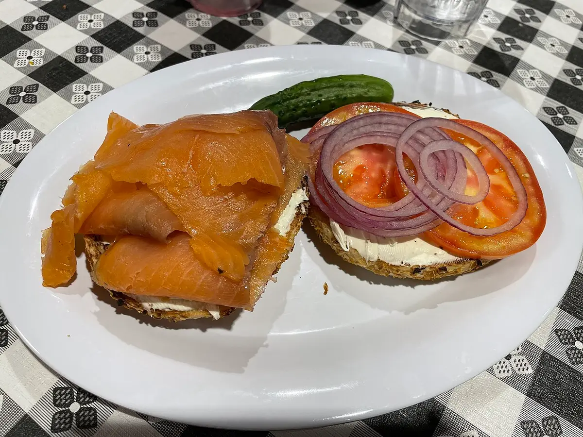An onion bagel with cream cheese, smoked salmon, red onion and tomato, a pickle on the side