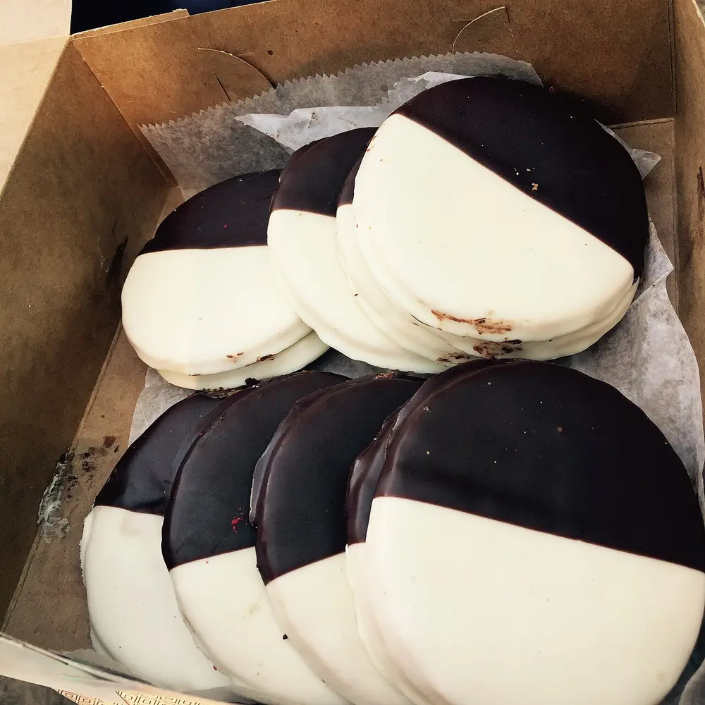 A box of black and white cookies, iced half in chocolate and half in vanilla