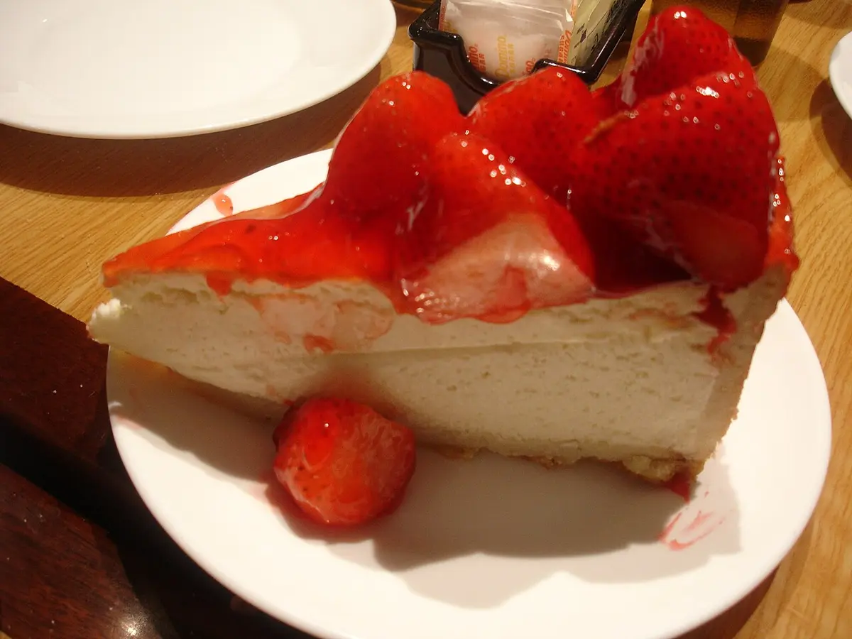 A tall slice of cheesecake topped with strawberries and glaze