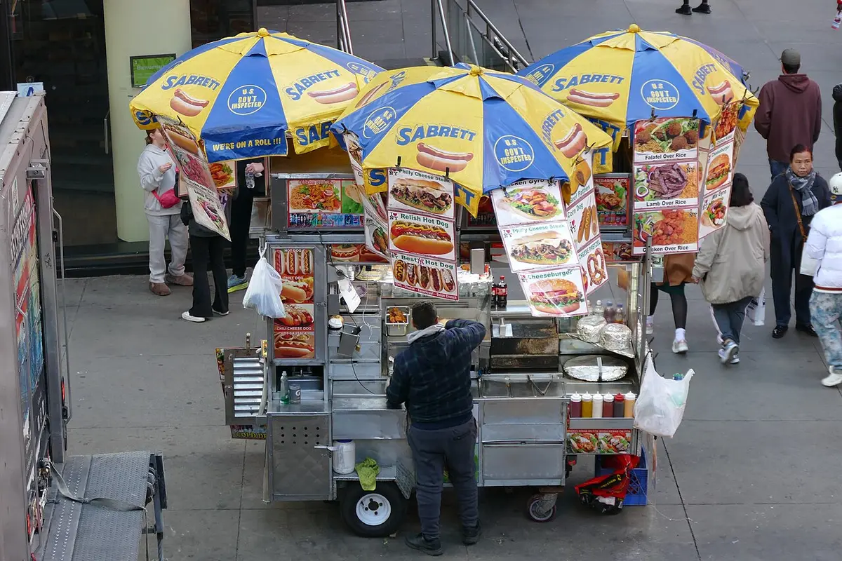 A hot dog cart under striped umbrellas on a Midtown sidewalk