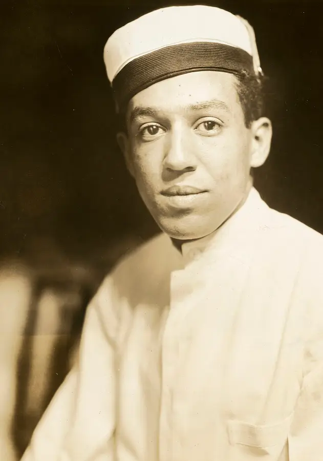 Sepia photograph of the young Langston Hughes in a white jacket and cap