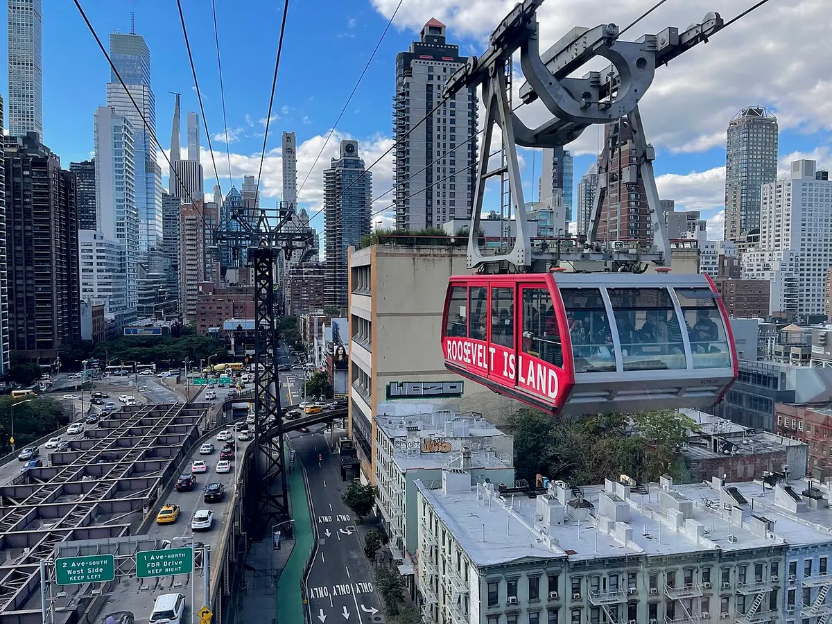 A red Roosevelt Island Tramway cabin high above the traffic of the East Side, Midtown towers behind