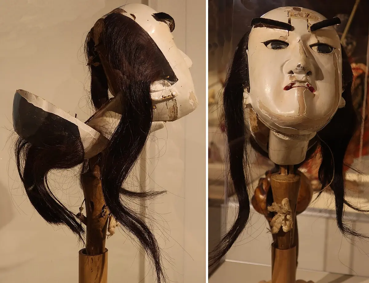 Two views of a carved male bunraku puppet head on its long wooden grip