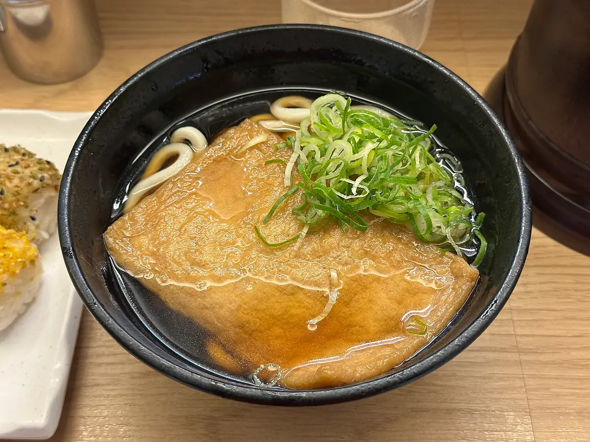A bowl of kitsune udon topped with a sheet of sweet fried tofu and green onion