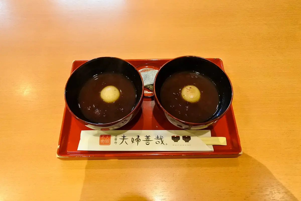 Two small lacquered bowls of sweet red bean soup on a red tray