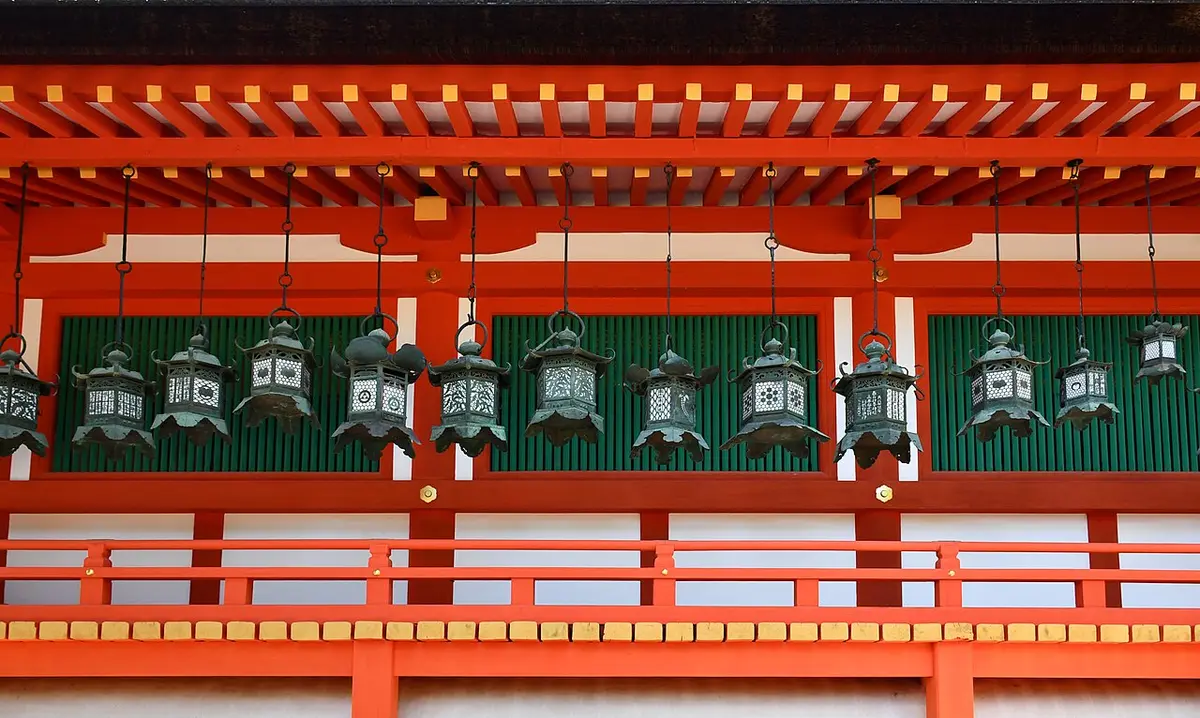 Rows of bronze hanging lanterns along a vermilion cloister at Kasuga Taisha