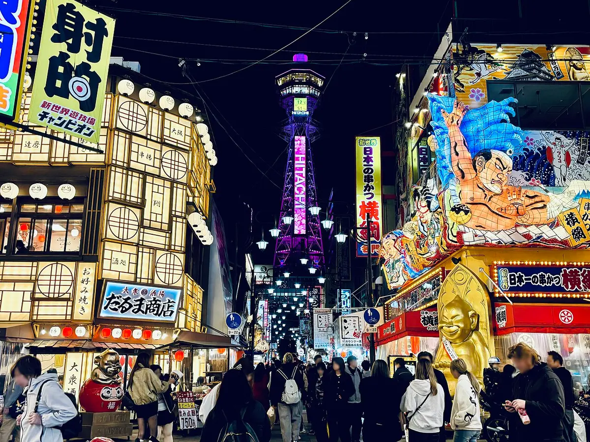 A street in Shinsekai at night, restaurant signs and lanterns leading to the lit Tsūtenkaku tower