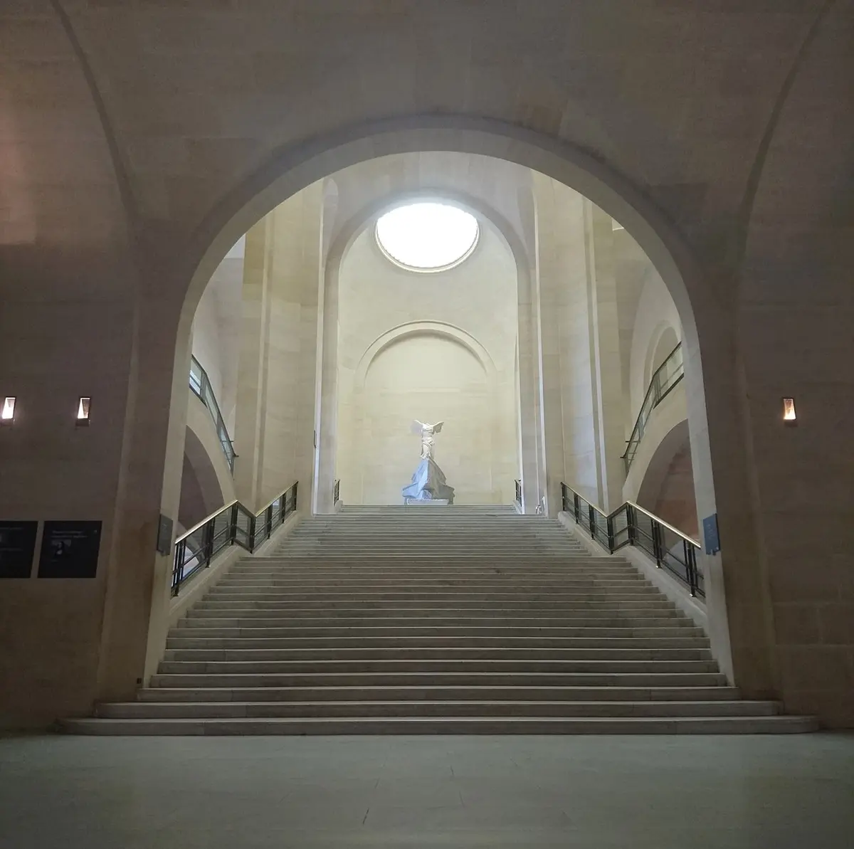 The Winged Victory of Samothrace at the top of a wide stone staircase under a skylight