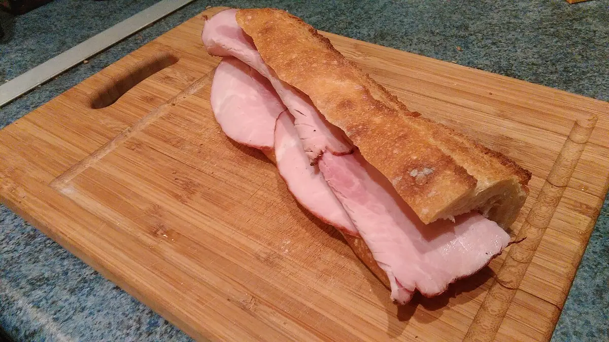 A baguette filled with ham and butter on a wooden board