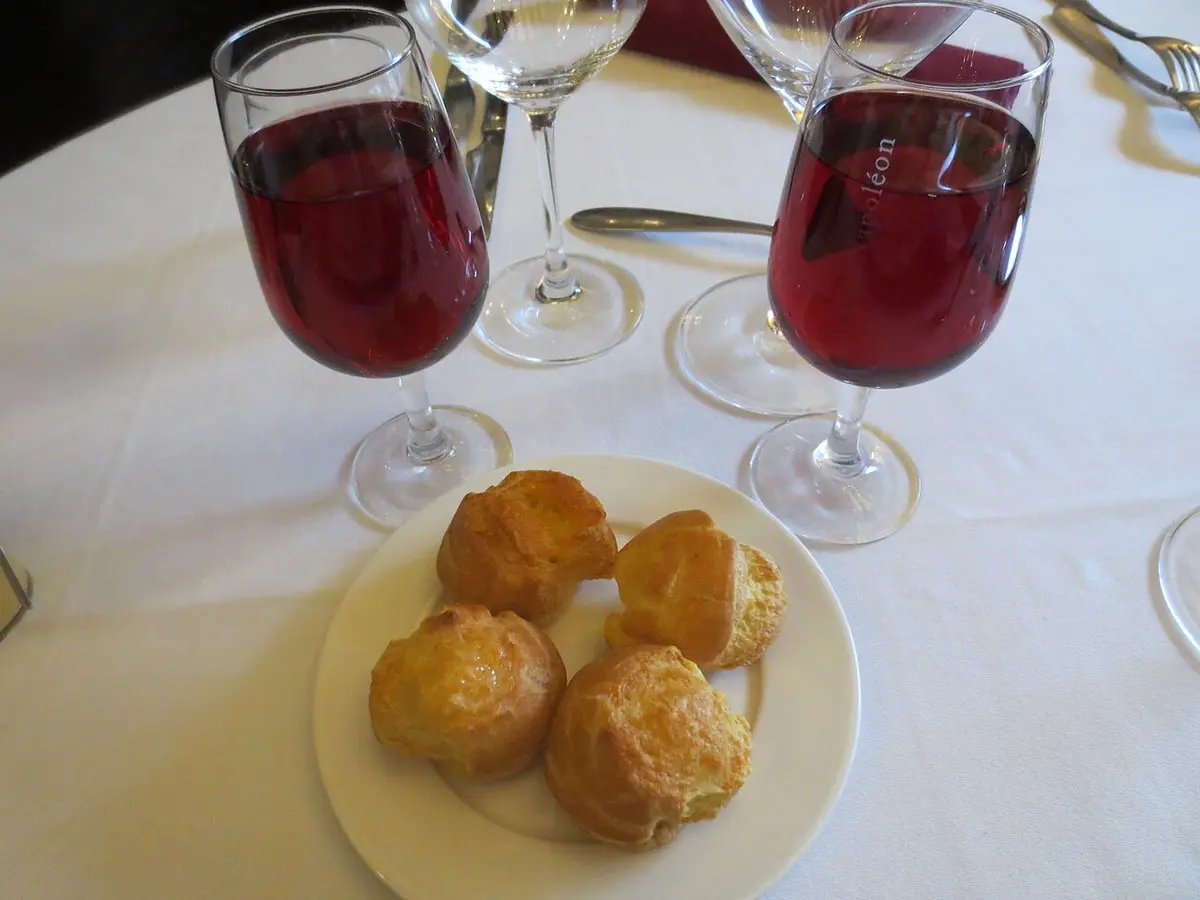 Two glasses of kir on a white tablecloth beside a plate of small cheese puffs