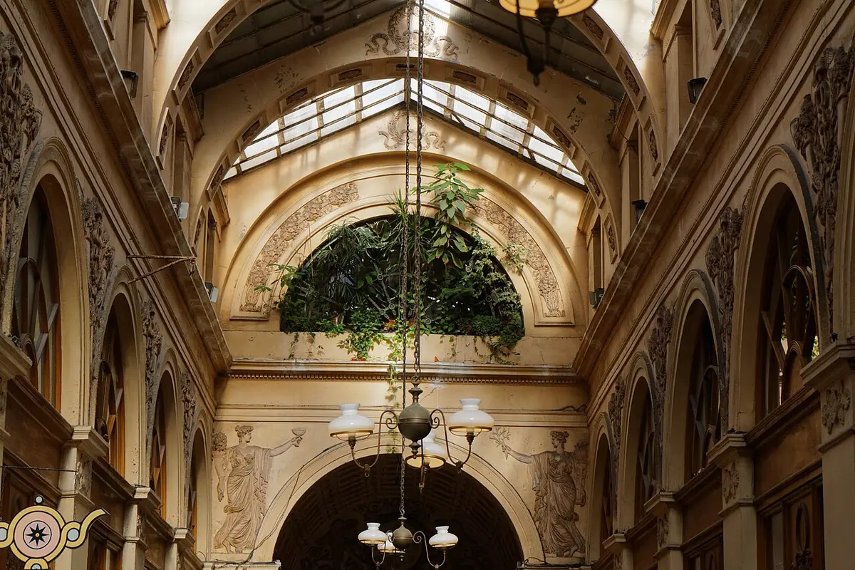 Carved arches, painted figures, hanging plants and glass lamps under the roof of the Galerie Vivienne