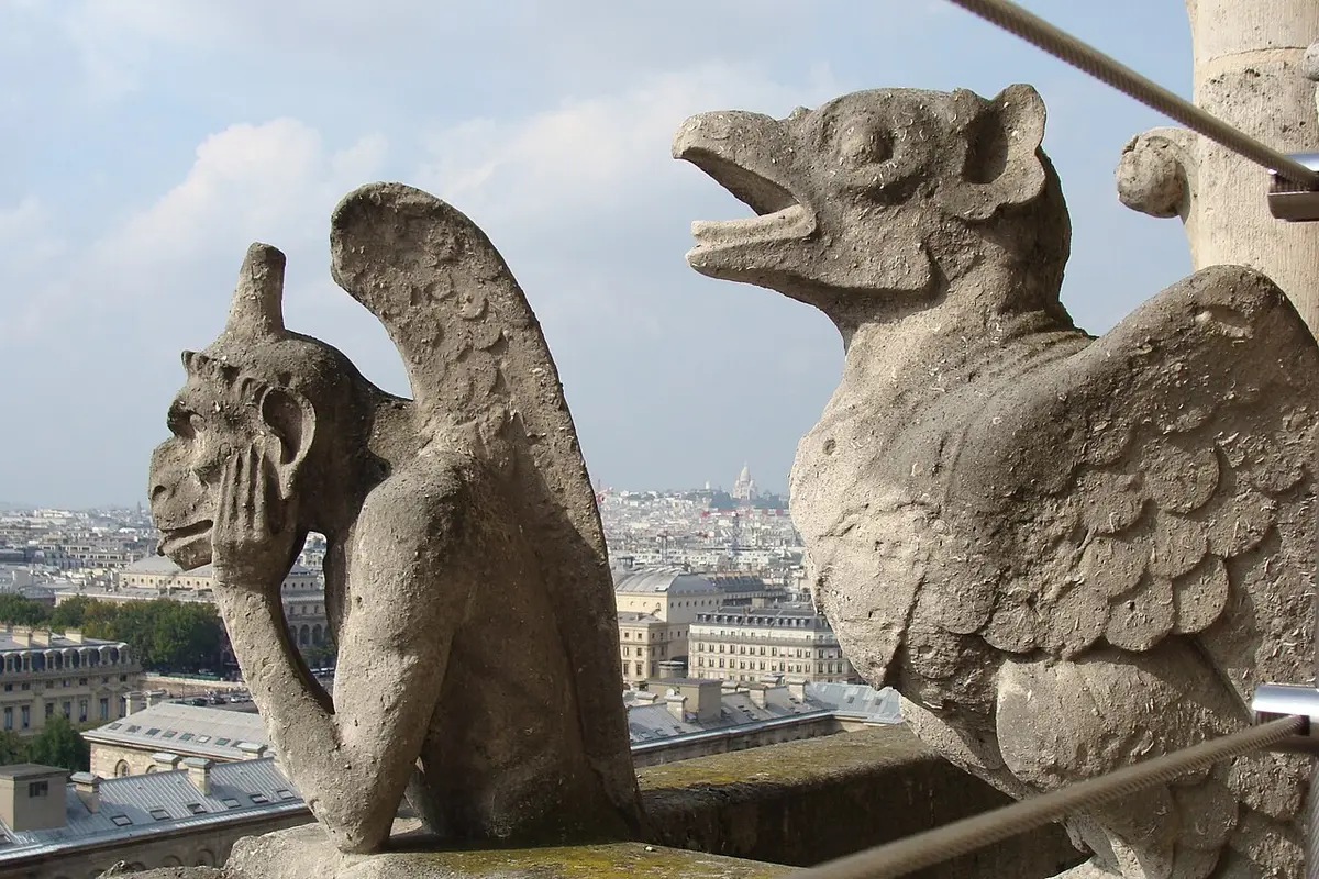 Two stone chimeras on Notre-Dame, one with its chin in its hands, above the rooftops of Paris