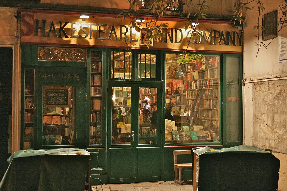 The green wooden front of the Shakespeare and Company bookshop, lit at night, books stacked in the windows